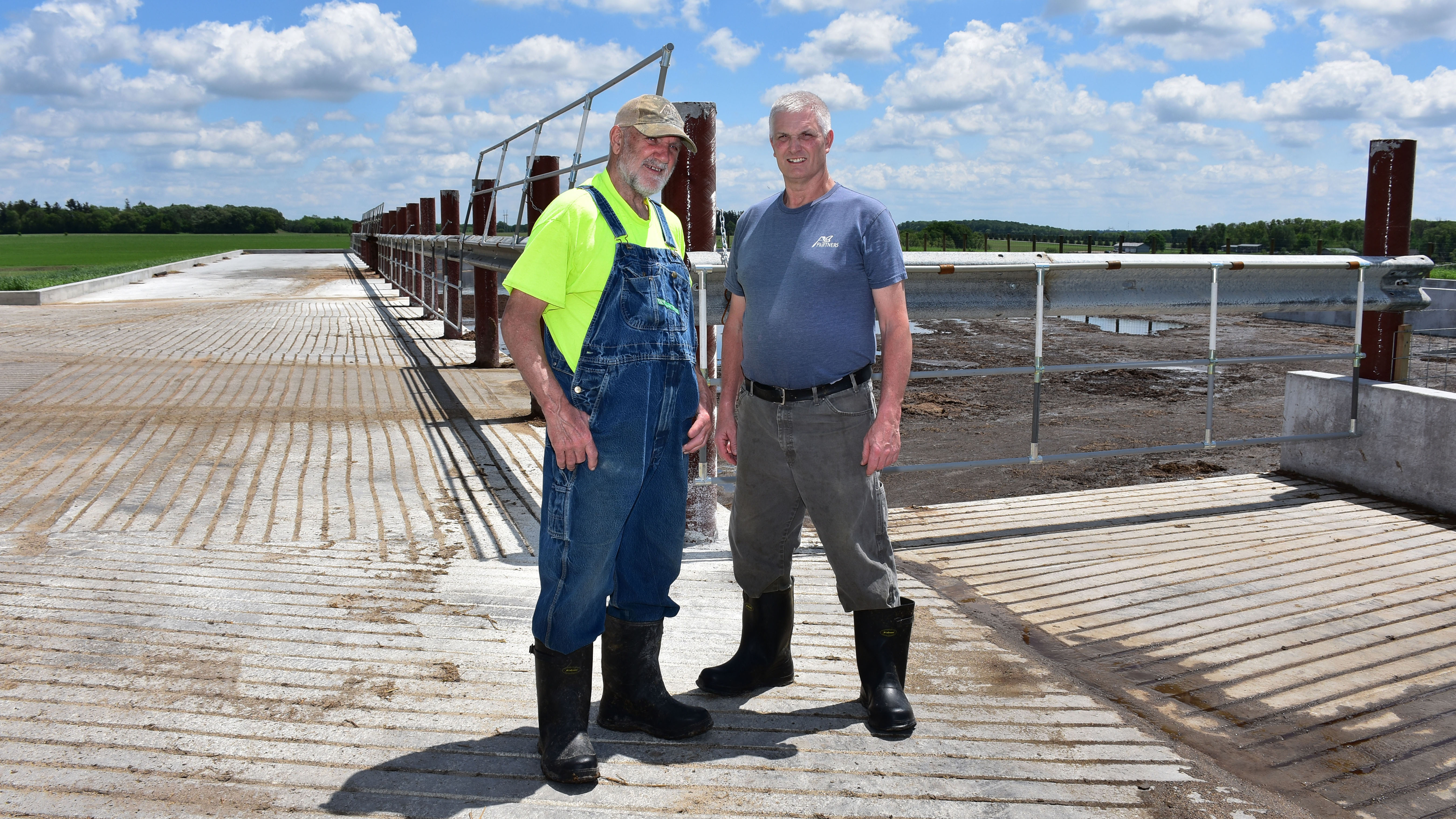 Jay Currier and Ben Currier stand at the corner of their new manure pit, which is enclosed by a fence.