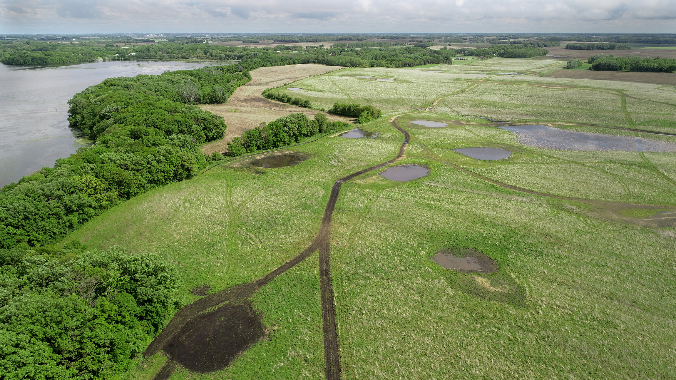 Small wetlands appear amid green and trees border a lake at left