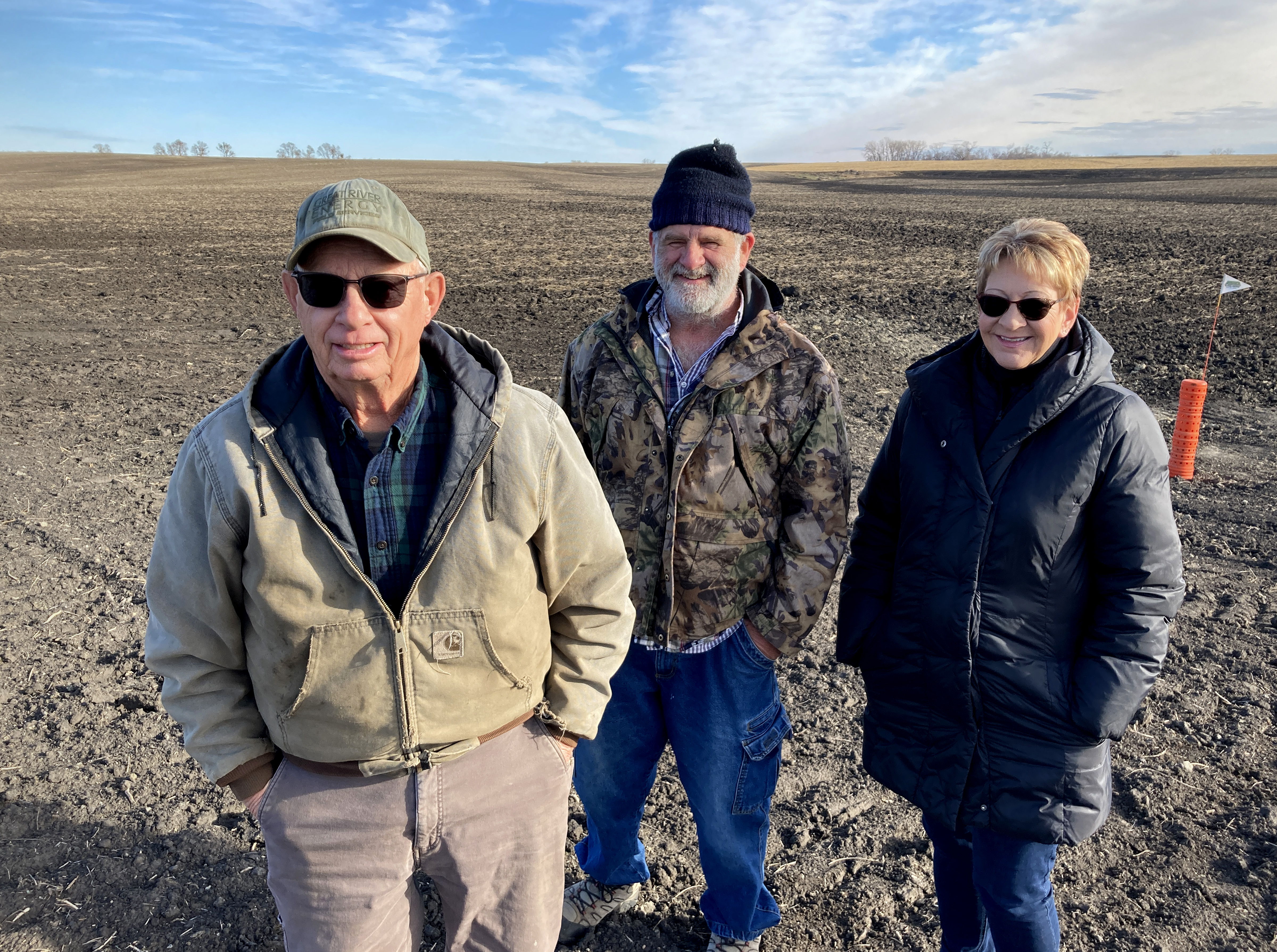 Three people stand in a field where black dirt shows construction has recently taken place