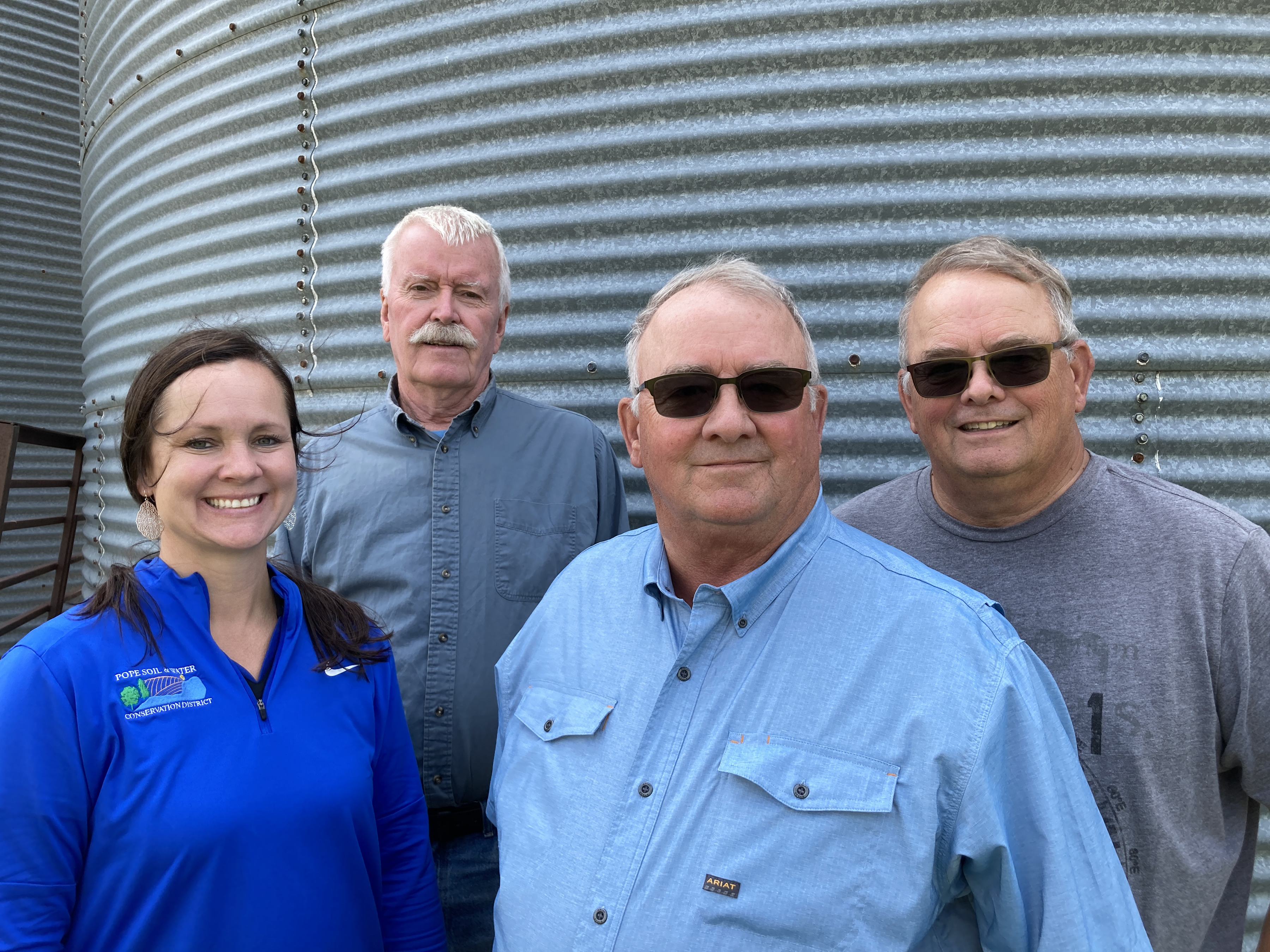 four people stand in front of a grain bin