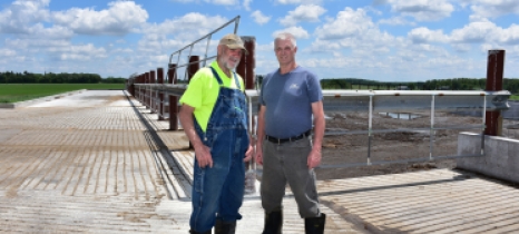 Jay Currier and Ben Currier stand at the corner of their new manure pit, which is enclosed by a fence.