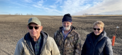 Three people stand in a field where black dirt shows construction has recently taken place
