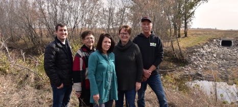 Five people stand in a group with a creek and a large square culvert in the background