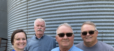 four people stand in front of a grain bin
