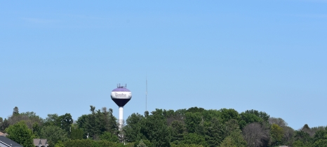 water tower behind trees, a highway and a corn field