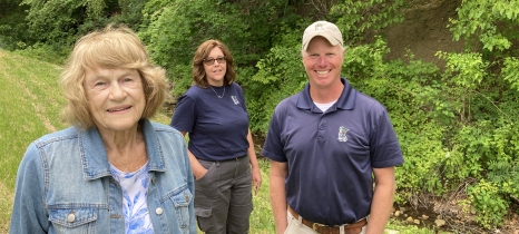 A group of three people stand in a farm field