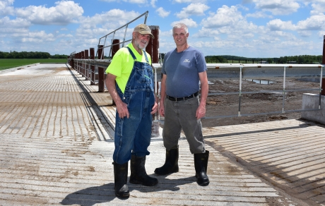 Jay Currier and Ben Currier stand at the corner of their new manure pit, which is enclosed by a fence.