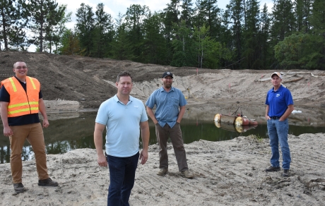 Four men stand in front of a pond filled with water
