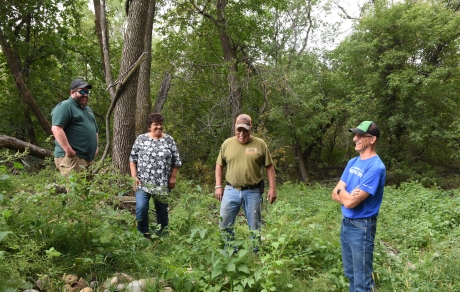Four people stand in green plants with trees in the background