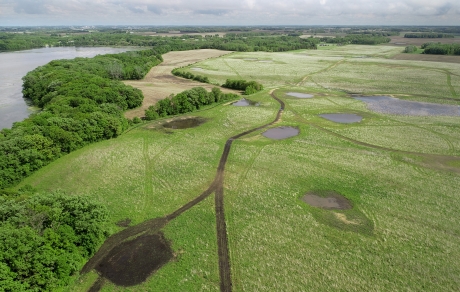 Small wetlands appear amid green and trees border a lake at left