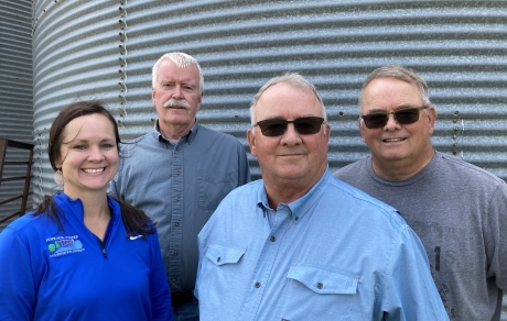 four people stand in front of a grain bin