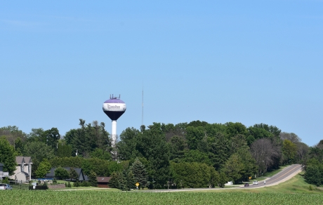 water tower behind trees, a highway and a corn field