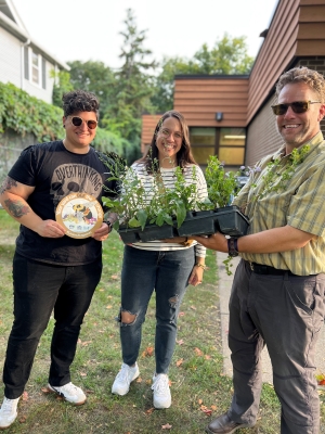 Three people stand together holding native plant plugs and a L2L garden sign